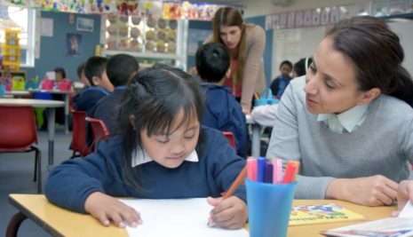 Teaching working at school desk with child who is writing